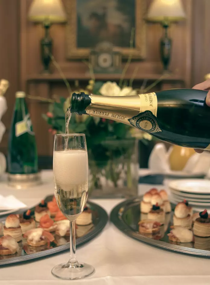 Champagne being poured into a flute before a table with assorted hors d’oeuvres