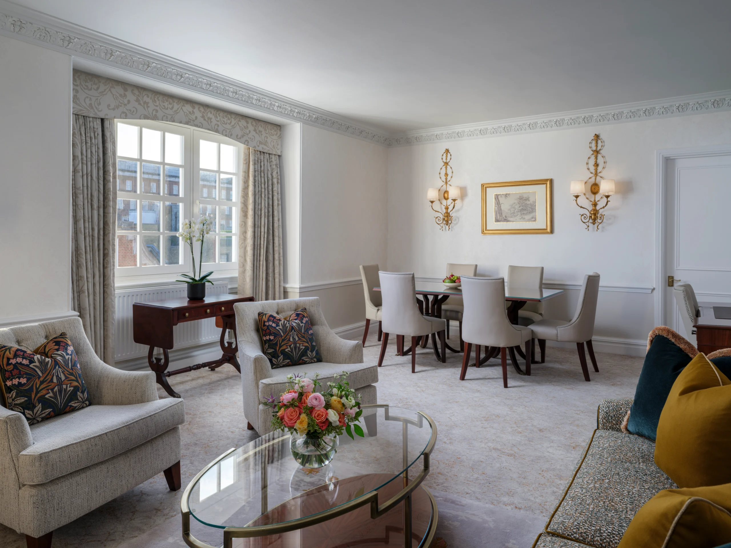 Large living room with grey sofas, flowers on the coffee table, dining table, armchairs, window treatments and art on walls