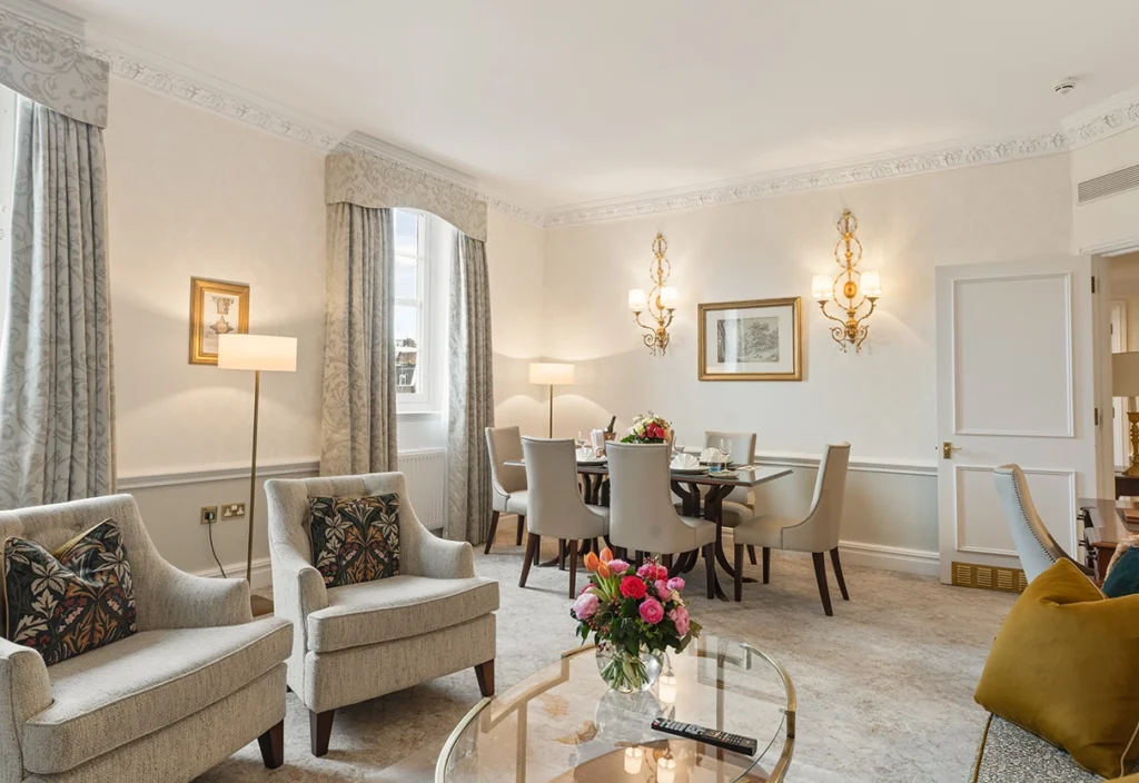 Large living room with grey sofas, flowers on the coffee table, dining table, armchairs, window treatments and art on walls